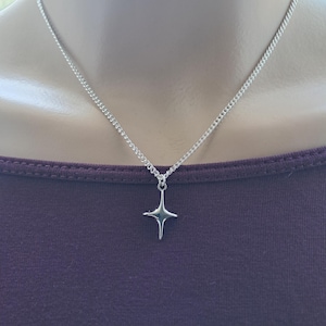 May include: A silver-colored necklace with a four-pointed star pendant. The chain is a delicate curb style, and the pendant has a polished finish. The necklace is displayed against a dark purple background.