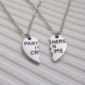 May include: Two silver necklaces with heart-shaped pendants that say "PARTNERS IN CRIME".