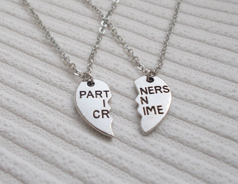 May include: Two silver necklaces with heart-shaped pendants that say "PARTNERS IN CRIME".
