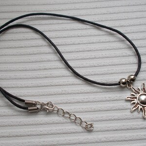 May include: A silver sun pendant necklace with a black cord. The sun pendant has a detailed design with rays extending outwards. The necklace includes a silver clasp and adjustable chain.