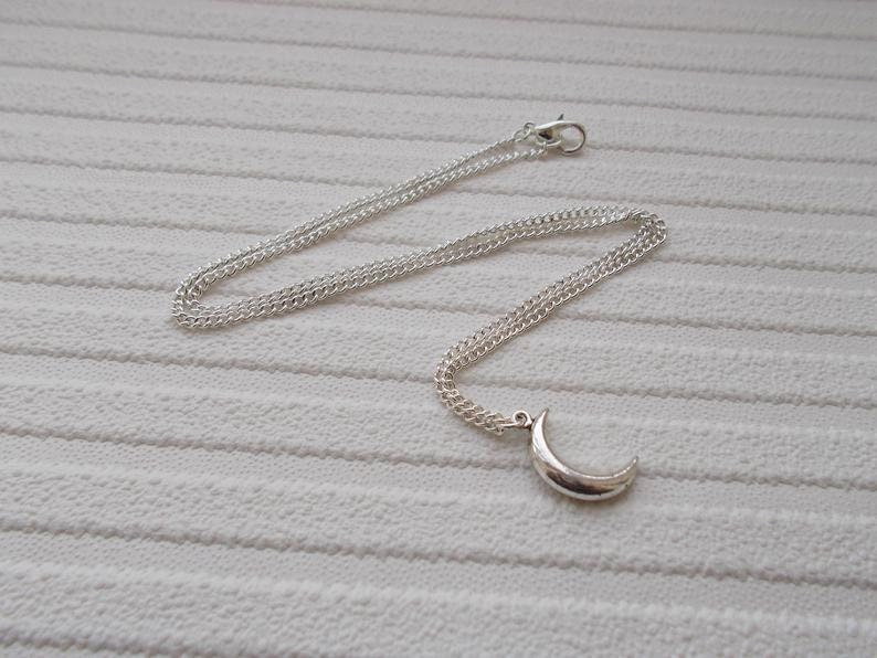 Pu&ograve; includere: Collana color argento con un ciondolo a forma di mezzaluna. La catena sottile &egrave; collegata a una chiusura a moschettone. Il ciondolo a forma di luna &egrave; liscio e curvo.