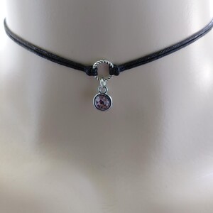 May include: A black choker necklace with a silver-colored ring and a small, round, pink gemstone pendant. The necklace is made of two strands of black cord.