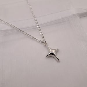 May include: A silver-colored necklace with a four-pointed star pendant. The chain is a delicate curb link style. The pendant has a smooth, reflective surface. The necklace is displayed on a white background.