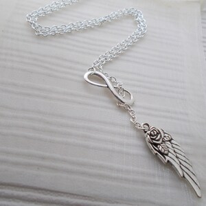 Pu&ograve; includere: Collana color argento con un simbolo dell'infinito e un ciondolo a forma di ala con un dettaglio a rosa. La catena &egrave; delicata e il ciondolo &egrave; finemente lavorato. La collana &egrave; esposta su una superficie bianca e strutturata.