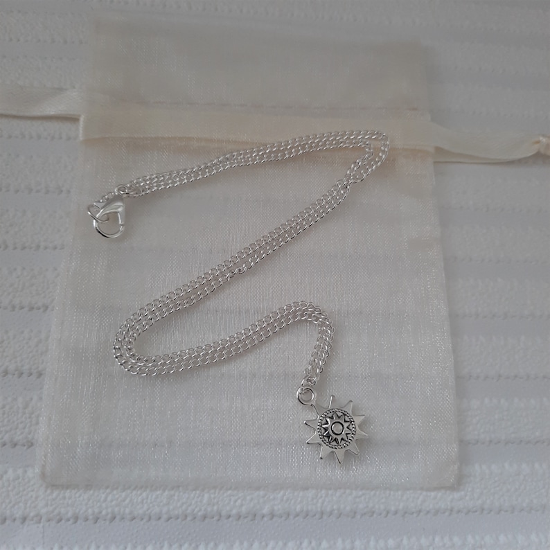 May include: A silver chain necklace with a silver star pendant. The star has a detailed design and is hanging from a silver chain.