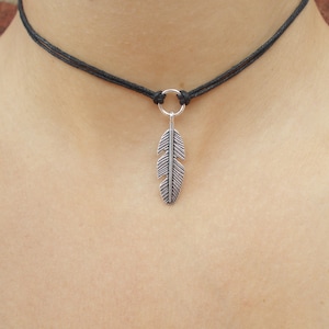 May include: A black cord choker necklace with a silver feather pendant.