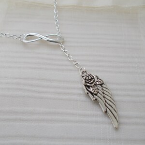 Pu&ograve; includere: Collana color argento con un simbolo dell'infinito e un ciondolo con un'ala e un design a rosa. La collana ha una catena delicata ed &egrave; esposta su uno sfondo morbido e neutro.