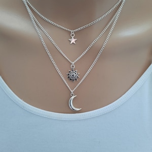 May include: A silver layered necklace with a crescent moon, sun, and star pendant.