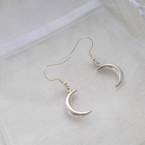 Pu&ograve; includere: Un paio di orecchini a mezzaluna color argento. Gli orecchini sono esposti su uno sfondo bianco. Gli orecchini hanno un design semplice ed elegante, con una forma curva che ricorda una mezzaluna.
