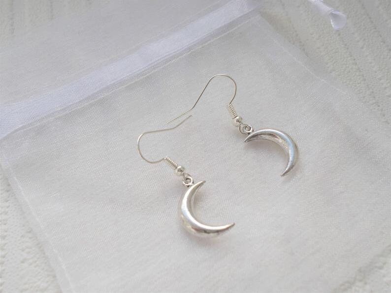 Pu&ograve; includere: Un paio di orecchini a mezzaluna color argento. Gli orecchini sono esposti su uno sfondo bianco. Gli orecchini hanno un design semplice ed elegante, con una forma curva che ricorda una mezzaluna.