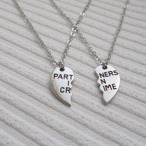 May include: Two silver necklaces with matching heart pendants that say "PARTNERS IN CRIME" on them. The hearts are broken in half and fit together.