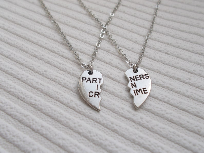 May include: Two silver necklaces with matching heart pendants that say "PARTNERS IN CRIME" on them. The hearts are broken in half and fit together.