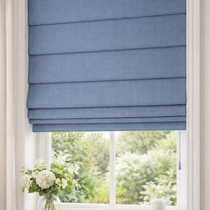 Puede incluir: Una persiana romana azul está instalada en un marco de ventana blanco. La persiana está hecha de una tela texturizada y está parcialmente bajada. Un jarrón de flores blancas se encuentra en el alféizar de la ventana, junto con una pila de libros y una vela pequeña.