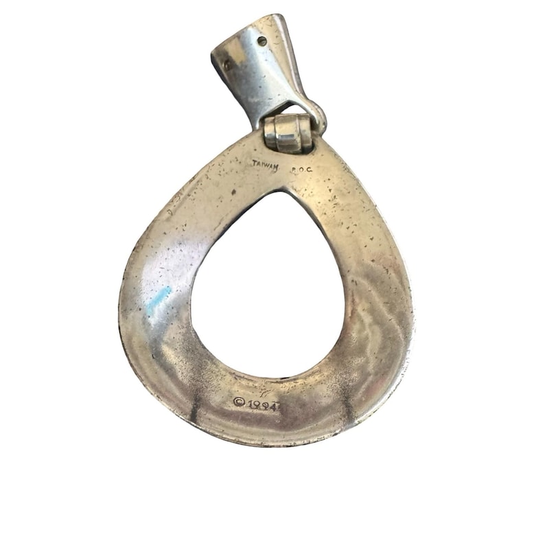 May include: Silver pendant with a teardrop design and a hinged bail. The pendant has a hollow centre and is marked with "TAIWAN R.O.C." and "&copy; 1994". The metal has a slightly tarnished appearance.