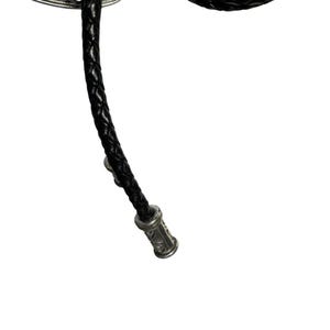K&ouml;nnte beinhalten: Nahaufnahme einer schwarzen geflochtenen Leder-Bolo-Krawatte. Die Krawatte hat einen silberfarbenen dekorativen Verschluss am Ende mit eingravierten Details. Die Bolo-Krawatte ist ein klassisches Accessoire.