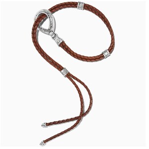 May include: A brown leather bolo tie with a silver clasp and accents. The braided leather cord forms a loop and two strands that end with decorative silver tips. The clasp has an oval shape with intricate detailing.