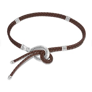May include: A brown leather necklace with a braided design. The necklace has silver-coloured metal accents and a decorative clasp. The design includes a knot-like feature in the centre, with two braided leather strands hanging down.