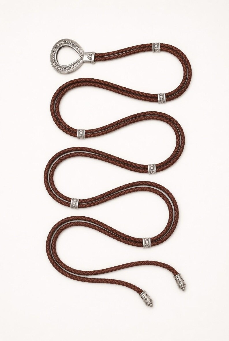 May include: A brown leather belt with a silver buckle and decorative accents. The braided belt has multiple silver embellishments. The buckle is a unique teardrop shape. The belt's length is approximately 100 cm.