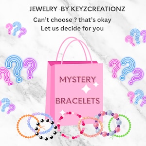 Könnte beinhalten: Rosa Einkaufstasche mit der Aufschrift "MYSTERY BRACELETS" und Fragezeichen. Mehrere Perlenarmbänder in verschiedenen Farben, darunter Orange, Blau, Rosa und Grün, werden vor der Tasche angezeigt. Der Text "JEWELRY BY KEYZCREATIONZ" steht oben.