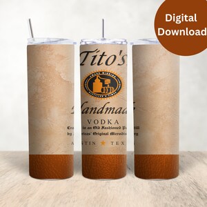 Pu&ograve; includere: Un set di tre bicchieri in acciaio inossidabile con un design che presenta il logo e il testo di Tito's Vodka. I bicchieri hanno una texture in pelle marrone nella parte inferiore e uno sfondo beige con un aspetto testurizzato.