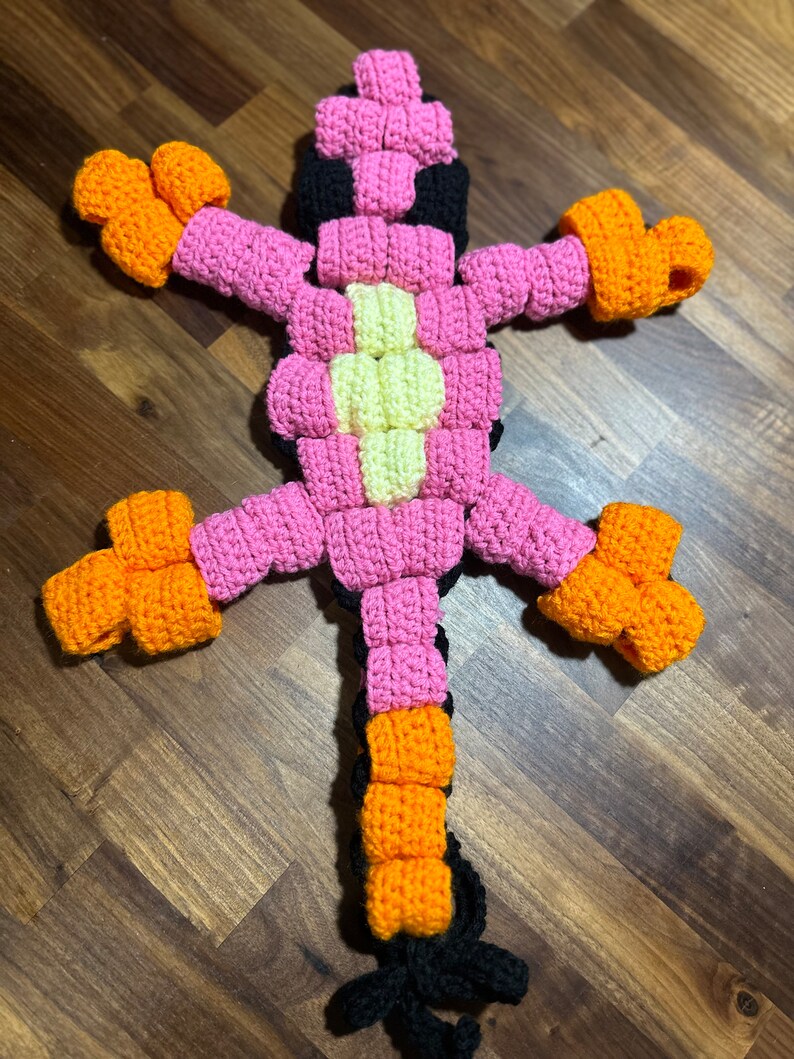 May include: A crocheted pink, orange and black lizard toy with a long tail.