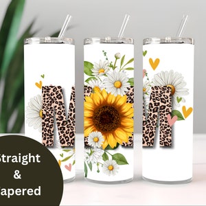 Könnte beinhalten: Drei Edelstahlbecher mit weißem Hintergrund und floralem Design. Die Becher zeigen eine Sonnenblume, Gänseblümchen und einen Leopardenmuster-Buchstaben "M".