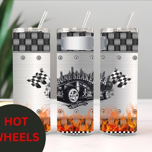 May include: A stainless steel tumbler with a checkered pattern and flames at the bottom. The tumbler features a Hot Wheels logo and a black and white illustration of a hot rod with the text "Bone Shaker".