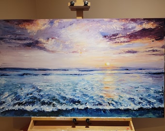 May include: An oil painting of a seascape with a sunset. The sky is a mix of purple, orange, and yellow hues, with the sun setting on the horizon. The ocean is a deep blue, with white waves crashing on the shore. The painting is displayed on an easel.
