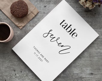 May include: White table number card with black text. The card says "table seven" and "Thomas and Mary 11.17.2021".