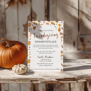 Op de afbeelding: Een Friendsgiving-dinerpotluck-uitnodiging met herfstthema-illustraties. De uitnodiging bevat de evenementdetails: datum, tijd en locatie. Een pompoen en kalebas liggen op een houten oppervlak.