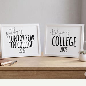 May include: Two white framed prints on a wooden surface. The left print reads "first day of JUNIOR YEAR IN COLLEGE 2026" in black script. The right print reads "third year of COLLEGE 2026". A small succulent in a white pot is visible.