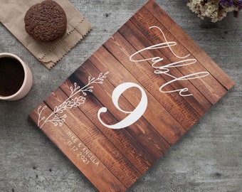 May include: Rustic wooden table number card with a white handwritten 'Table' and the number '9' in a white script font. The card also includes the names 'Mike & Angela' and the date '11.17.2021' in a white script font.