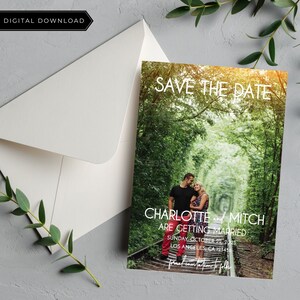 K&ouml;nnte beinhalten: Save-the-Date-Karte mit einem Foto eines Paares, das auf einem Bahngleis in einem Wald steht. Der Text auf der Karte lautet "Save the Date, Charlotte und Mitch heiraten, Sonntag, 22. Oktober 2023, Los Angeles, CA 123456".