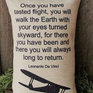 May include: A beige pillow with a black silhouette of a vintage airplane and a quote by Leonardo Da Vinci: "Once you have tasted flight, you will walk the Earth with your eyes turned skyward, for there you have been and there you will always long to return."