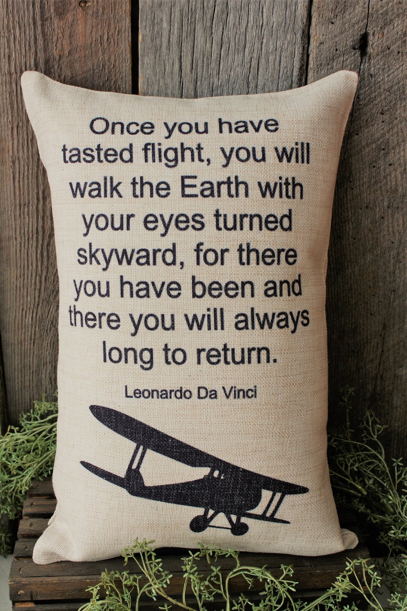 May include: A beige pillow with a black silhouette of a vintage airplane and a quote by Leonardo Da Vinci: "Once you have tasted flight, you will walk the Earth with your eyes turned skyward, for there you have been and there you will always long to return."