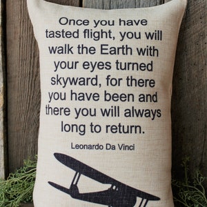 May include: A beige throw pillow with a black silhouette of a vintage airplane and a quote by Leonardo Da Vinci: "Once you have tasted flight, you will walk the Earth with your eyes turned skyward, for there you have been and there you will always long to return."