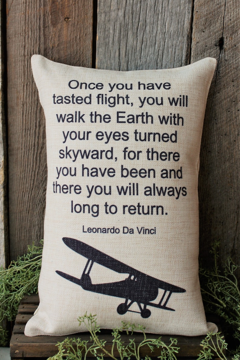 May include: A beige throw pillow with a black silhouette of a vintage airplane and a quote by Leonardo Da Vinci: "Once you have tasted flight, you will walk the Earth with your eyes turned skyward, for there you have been and there you will always long to return."