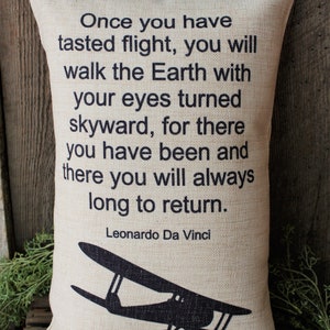 May include: A beige throw pillow with black text that reads "Once you have tasted flight, you will walk the Earth with your eyes turned skyward, for there you have been and there you will always long to return. Leonardo Da Vinci". A black silhouette of a vintage airplane is at the bottom of the pillow.