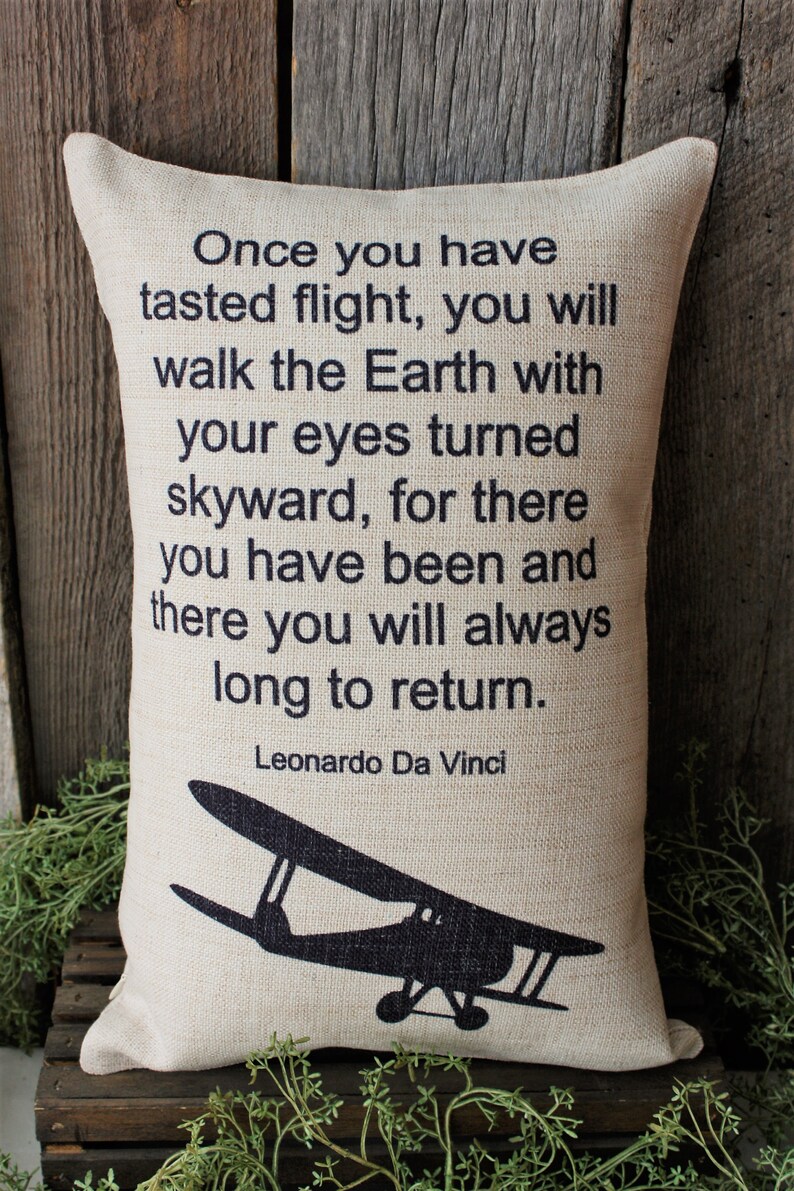 May include: A beige throw pillow with black text that reads "Once you have tasted flight, you will walk the Earth with your eyes turned skyward, for there you have been and there you will always long to return. Leonardo Da Vinci". A black silhouette of a vintage airplane is at the bottom of the pillow.
