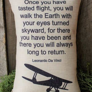 May include: A beige throw pillow with a black silhouette of a vintage airplane and a quote by Leonardo Da Vinci: "Once you have tasted flight, you will walk the Earth with your eyes turned skyward, for there you have been and there you will always long to return."