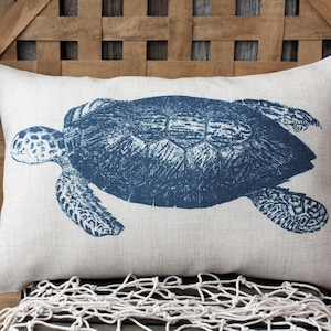 May include: A white pillow with a blue sea turtle design. The pillow is made of linen and has a subtle texture.