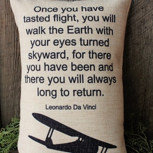 May include: A beige pillow with a black silhouette of a vintage airplane and a quote by Leonardo Da Vinci that reads: "Once you have tasted flight, you will walk the Earth with your eyes turned skyward, for there you have been and there you will always long to return."