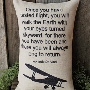 May include: A beige throw pillow with a black silhouette of a vintage airplane and a quote by Leonardo Da Vinci: "Once you have tasted flight, you will walk the Earth with your eyes turned skyward, for there you have been and there you will always long to return."
