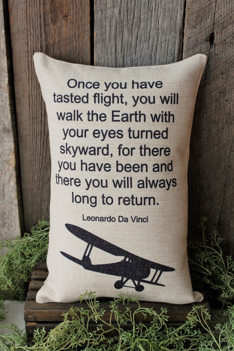 May include: A beige throw pillow with a black silhouette of a vintage airplane and a quote by Leonardo Da Vinci: "Once you have tasted flight, you will walk the Earth with your eyes turned skyward, for there you have been and there you will always long to return."