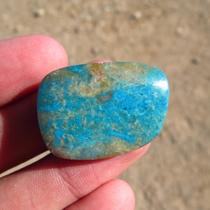 May include: A smooth, oval-shaped turquoise cabochon with a blue and brown marbled pattern.