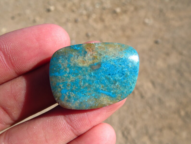 May include: A smooth, oval-shaped turquoise cabochon with a blue and brown marbled pattern.
