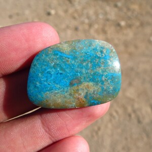 May include: A blue and green cabochon gemstone with a unique pattern. The stone is smooth and polished, and it has a natural, organic look.