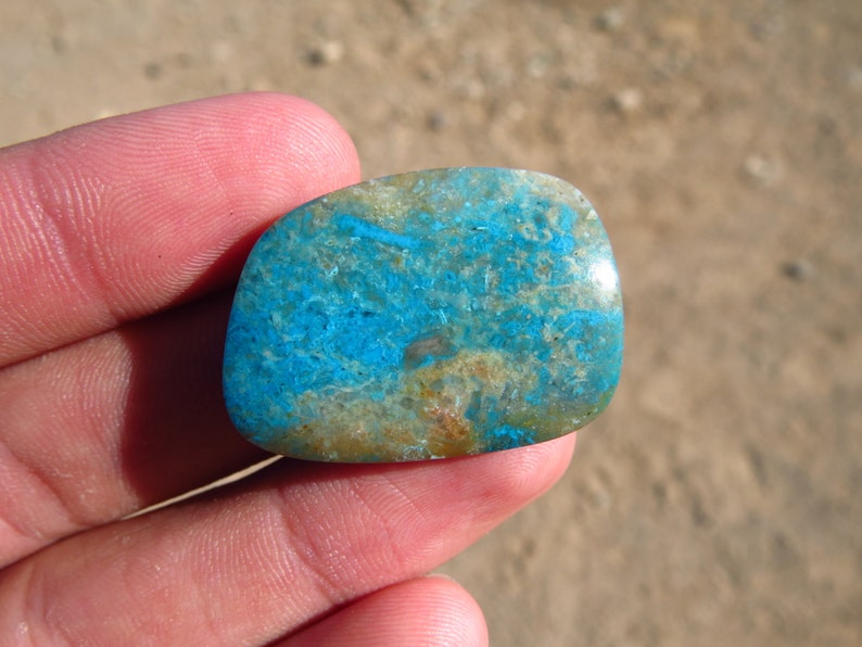 May include: A blue and green cabochon gemstone with a unique pattern. The stone is smooth and polished, and it has a natural, organic look.