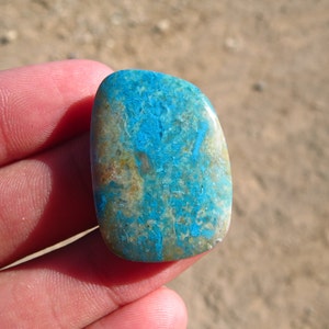 May include: An oval-shaped cabochon gemstone with a unique pattern of blue and brown. The stone is approximately 2.5 cm in length.