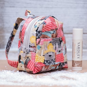 May include: A miniature, colorful fabric backpack with a zipper, patterned with various shapes and animal figures. A tube of Yardley lip balm is next to the backpack. The backpack has a handle and adjustable straps.